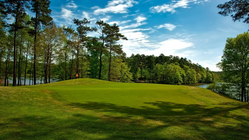 Beautiful golf course surrounded by trees and lake under a clear blue sky.