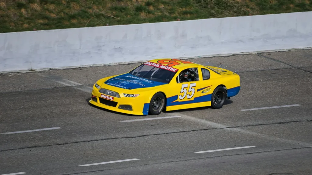 A vibrant yellow and blue stock car racing on an outdoor track during daytime.
