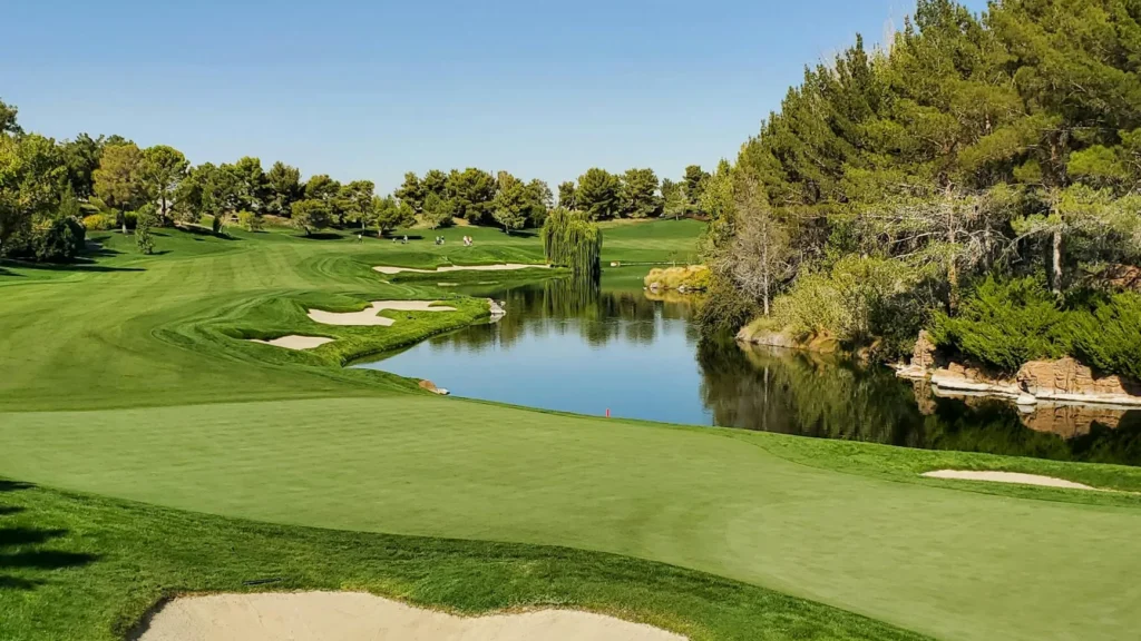 Experience a beautiful sunny day on a lush green golf course with a serene pond and sand trap.