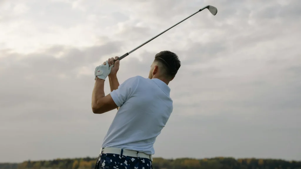 Back view of a golfer swinging a club outdoors on a cloudy day, showcasing the sport's precision and style.
