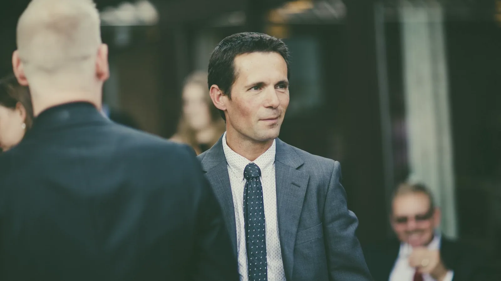 Business professional in tailored grey blazer and dress shirt networking at an upscale corporate hospitality event