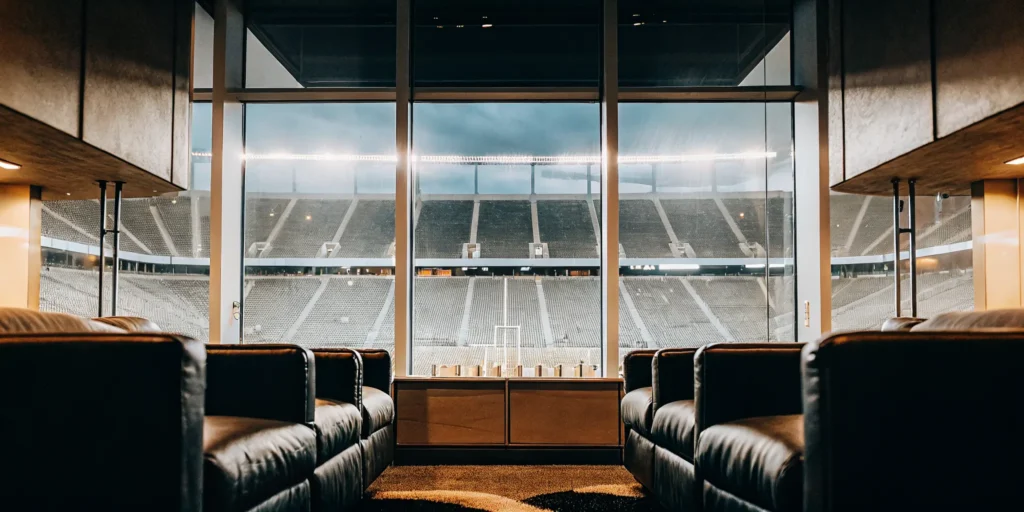 Luxury VIP suite inside a college football stadium with premium seating overlooking the field during a night game